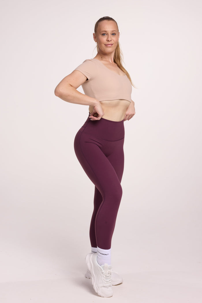 Buttery soft high waisted women's gym tights with curved back seam stitched detailing for a butt shaping effect, and no front rise seam, in plum purple paired with an V neck women's crop t-shirt with a supportive elasticated hem and triple layered fabric with removable pads for extra support in
beige