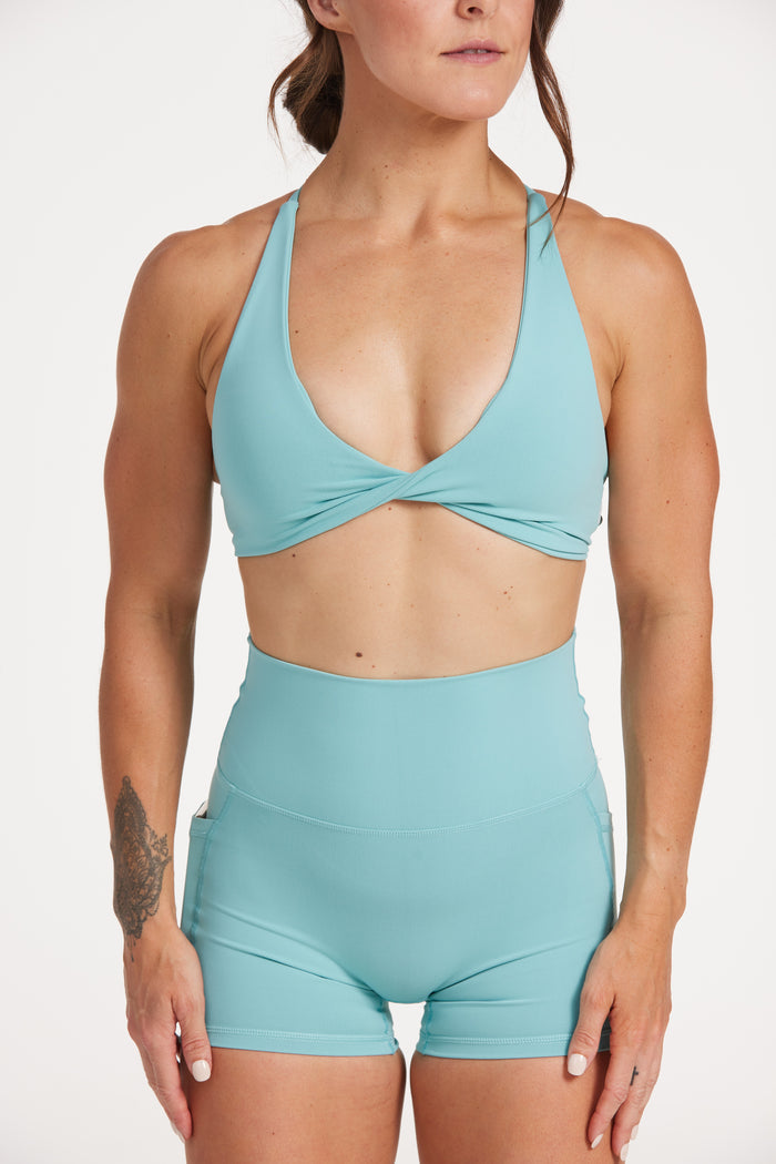 high waisted 4" inseam activewear pockets shorts with no front rise seam, in a buttery soft, supportive fabric with twist bra and cross over straps in lagoon green