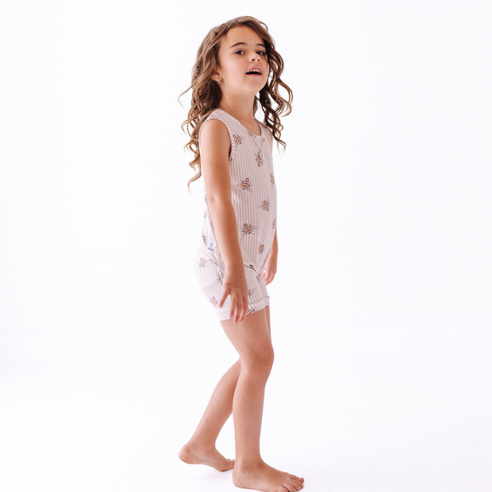 Girl wearing sleeveless romper with stripes and bees on a white background