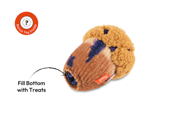 Play Berry Blast Muffin, a plush muffin-shaped dog toy with a tan fuzzy top, brown ribbed bottom, and dark blue accents, shown on a white background with text reading 'Fill Bottom with Treats' and a circular 'Bonus Toy Inside' badge.