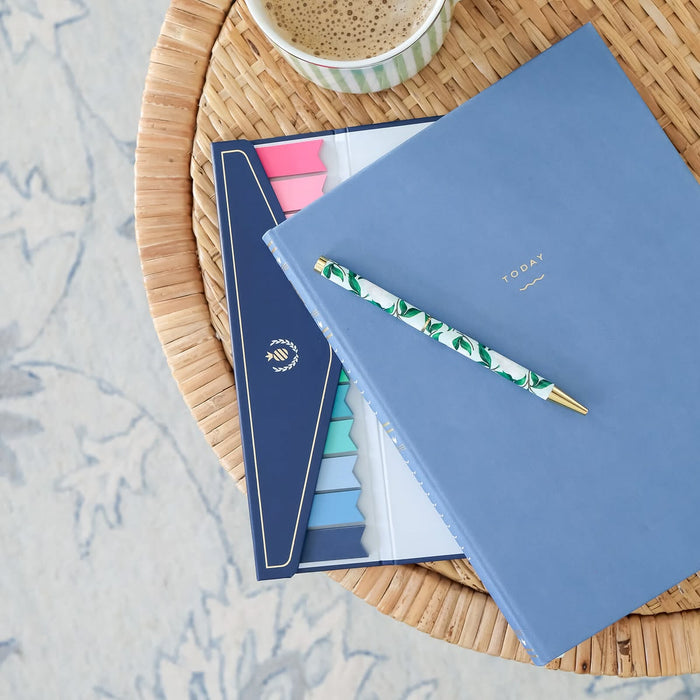 Blue notebook with a pen on a woven surface next to a cup of coffee