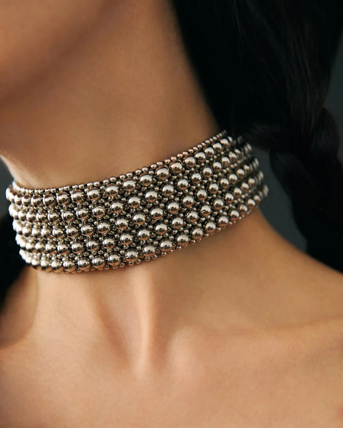 Woman wearing a silver choker against a dark background by object and dawn