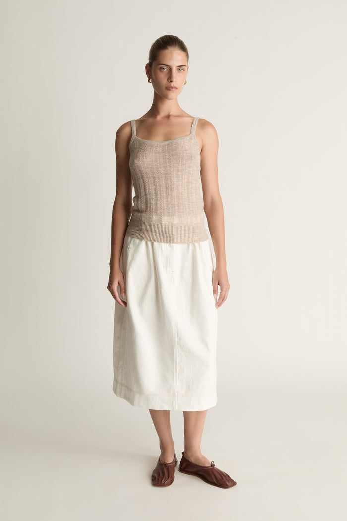 Woman wearing a beige tank top and white skirt on a plain background