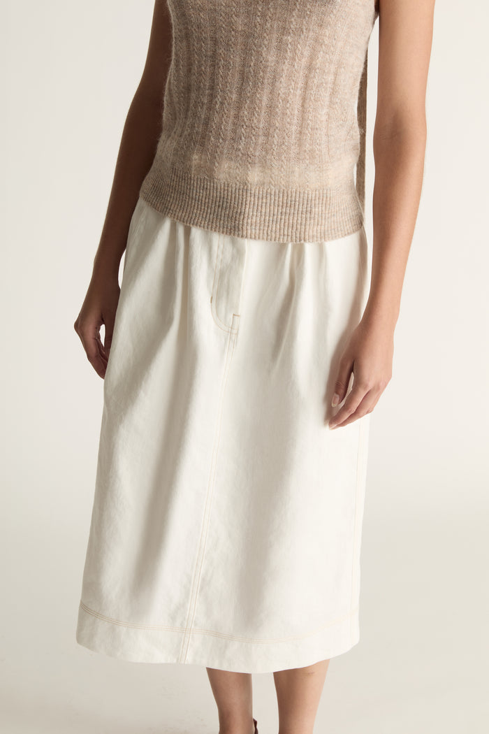 Woman wearing a beige tank top and white skirt on a plain background