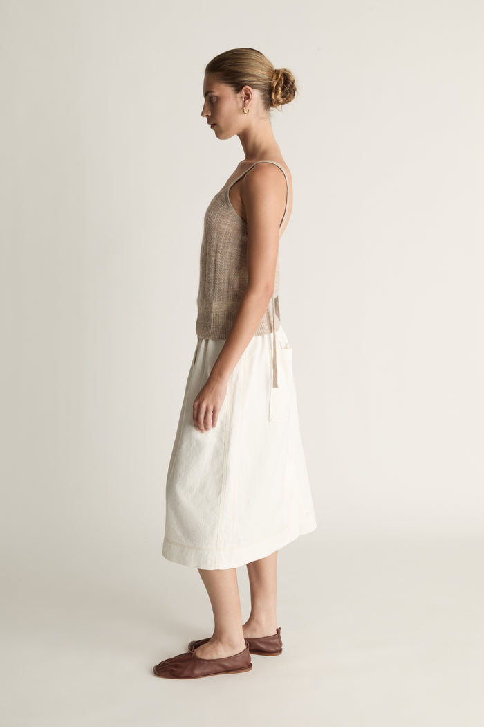 Woman wearing a beige tank top and white skirt on a plain background