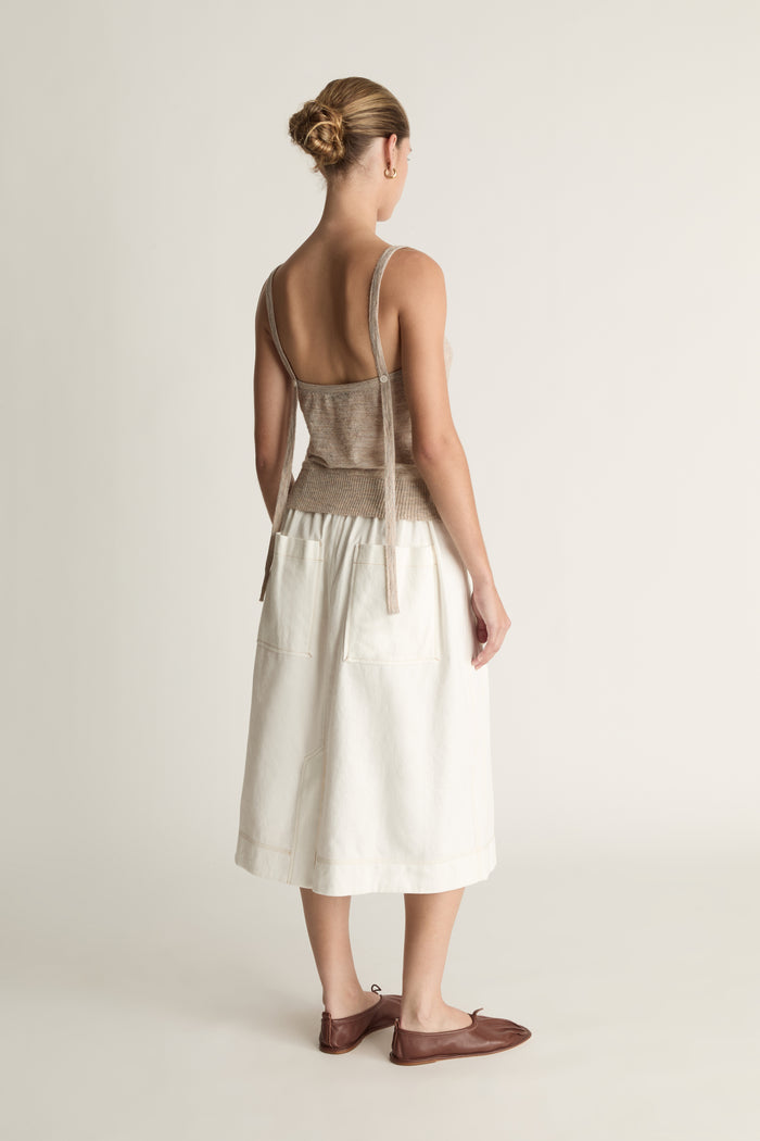 Woman wearing a beige tank top and white skirt on a plain background