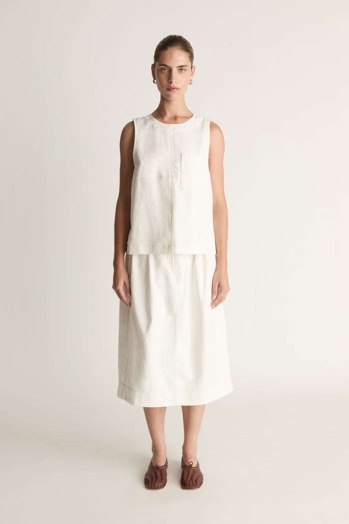 A woman wearing a white cami sleeveless tank top and a white skirt.