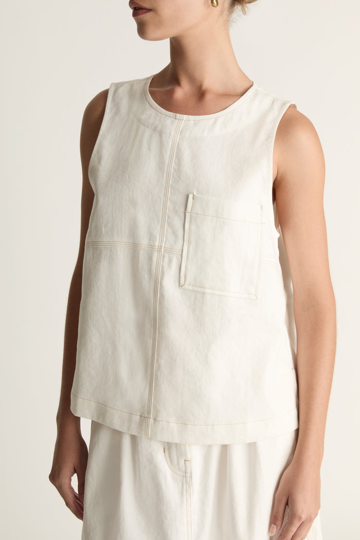 A woman wearing a white cami sleeveless tank top and a white skirt.