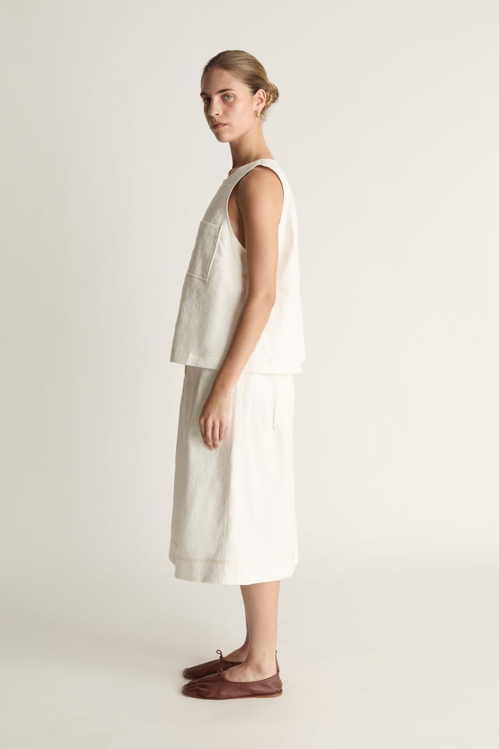 A woman wearing a white cami sleeveless tank top and a white skirt.