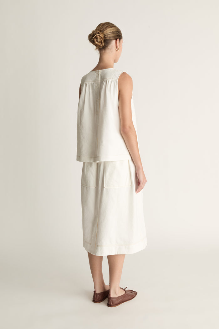 A woman wearing a white cami sleeveless tank top and a white skirt.