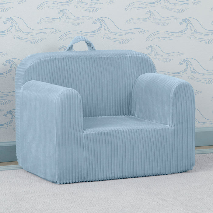A blue corduroy chair with a carry handle, placed in a room with a matching blue wallpaper.
