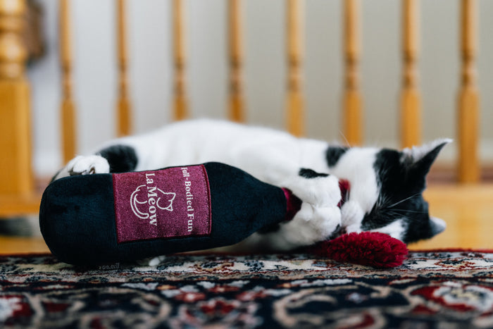 Cat playing with P.L.A.Y. Feline Frenzy Catbernet Sauv Kicker Toy on a patterned rug