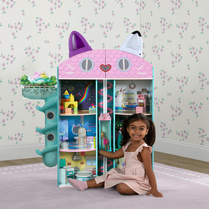 Child playing with a colorful toy cat house in a room with floral wallpaper.