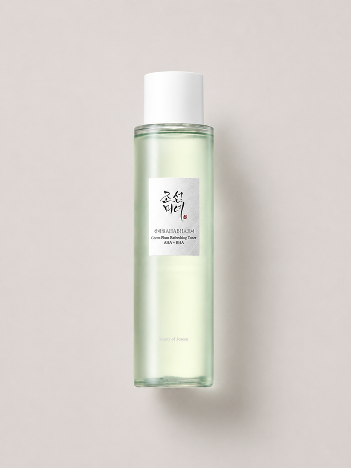 A clear glass bottle of Korean skincare toner with a white cap, containing a pale green liquid, set against a solid light beige background. Beauty of Joseon green plum Refreshing Toner AHA + BHA, 150 ml.