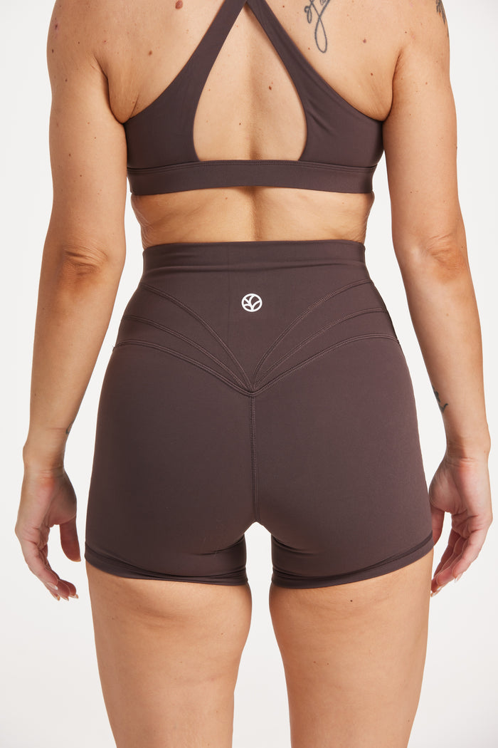 Buttery soft high waisted women's gym shorts with 4" inseam with curved stitched detailing for a butt shaping effect, and no front rise seam, paired with a high neck women's sports bra with a supportive elasticated hem and triple layered fabric with removable pads for extra support and crossover back straps in Dark Chocolate.