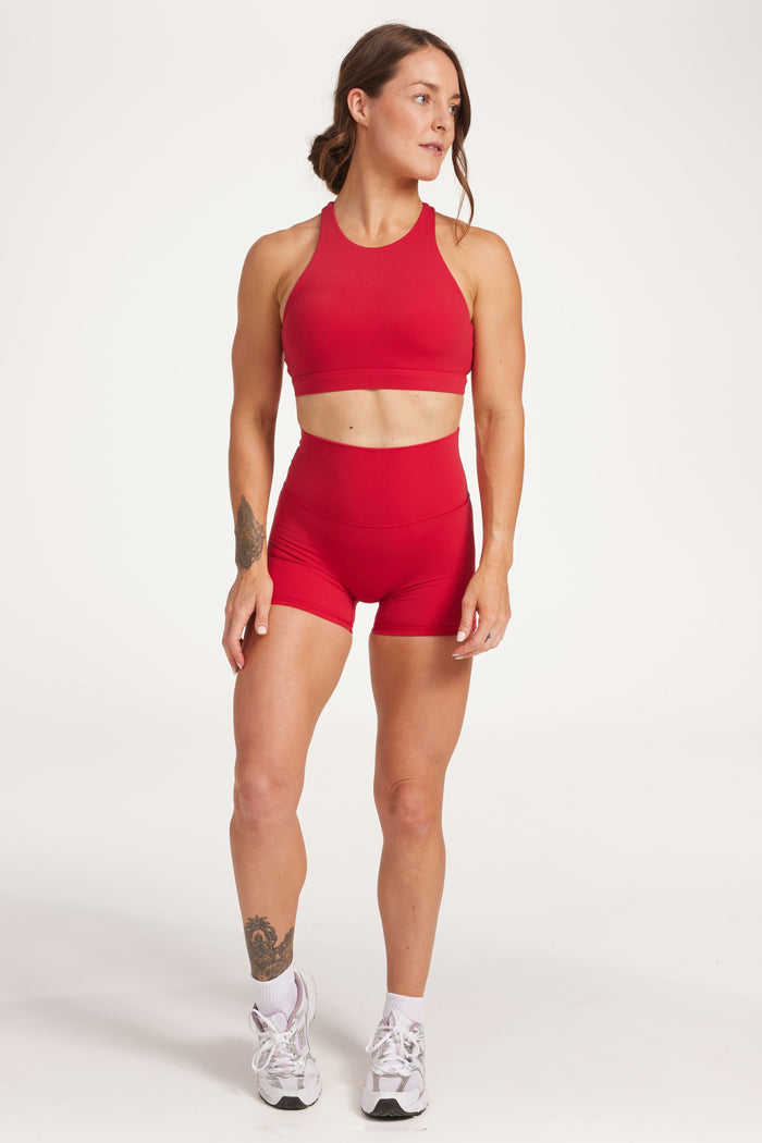 Buttery soft high waisted women's gym shorts with 4" inseam with curved stitched detailing for a butt shaping effect, and no front rise seam, paired with a high neck women's sports bra with a supportive elasticated hem and triple layered fabric with removable pads for extra support and crossover back straps in Raspberry red.