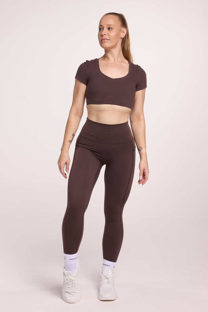 Buttery soft high waisted women's gym tights with practical pockets, sweetheart back seams for an upper glute shaping effect, and no front rise seam, paired with an V neck women's crop t-shirt with a supportive elasticated hem and triple layered fabric with removable pads for extra support in chocolate