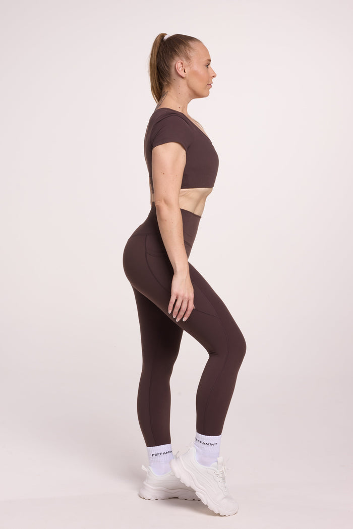 Buttery soft high waisted women's gym tights with practical pockets, sweetheart back seams for an upper glute shaping effect, and no front rise seam, paired with an V neck women's crop t-shirt with a supportive elasticated hem and triple layered fabric with removable pads for extra support in chocolate