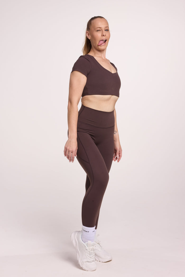 Buttery soft high waisted women's gym tights with practical pockets, sweetheart back seams for an upper glute shaping effect, and no front rise seam, paired with an V neck women's crop t-shirt with a supportive elasticated hem and triple layered fabric with removable pads for extra support in chocolate