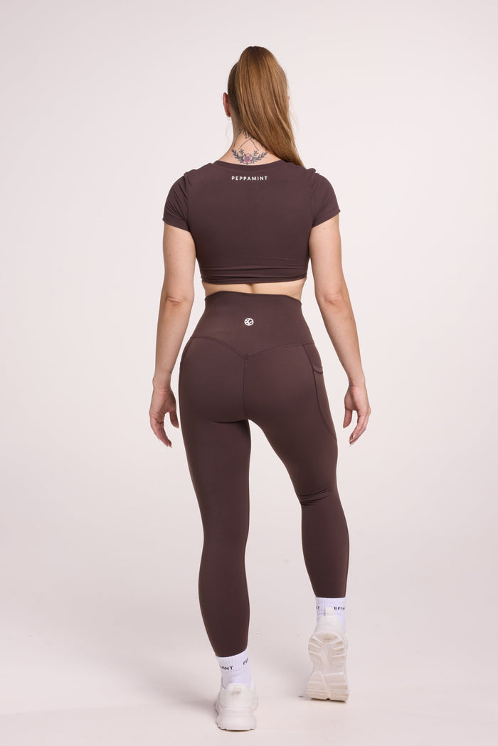 Buttery soft high waisted women's gym tights with practical pockets, sweetheart back seams for an upper glute shaping effect, and no front rise seam, paired with an V neck women's crop t-shirt with a supportive elasticated hem and triple layered fabric with removable pads for extra support in chocolate