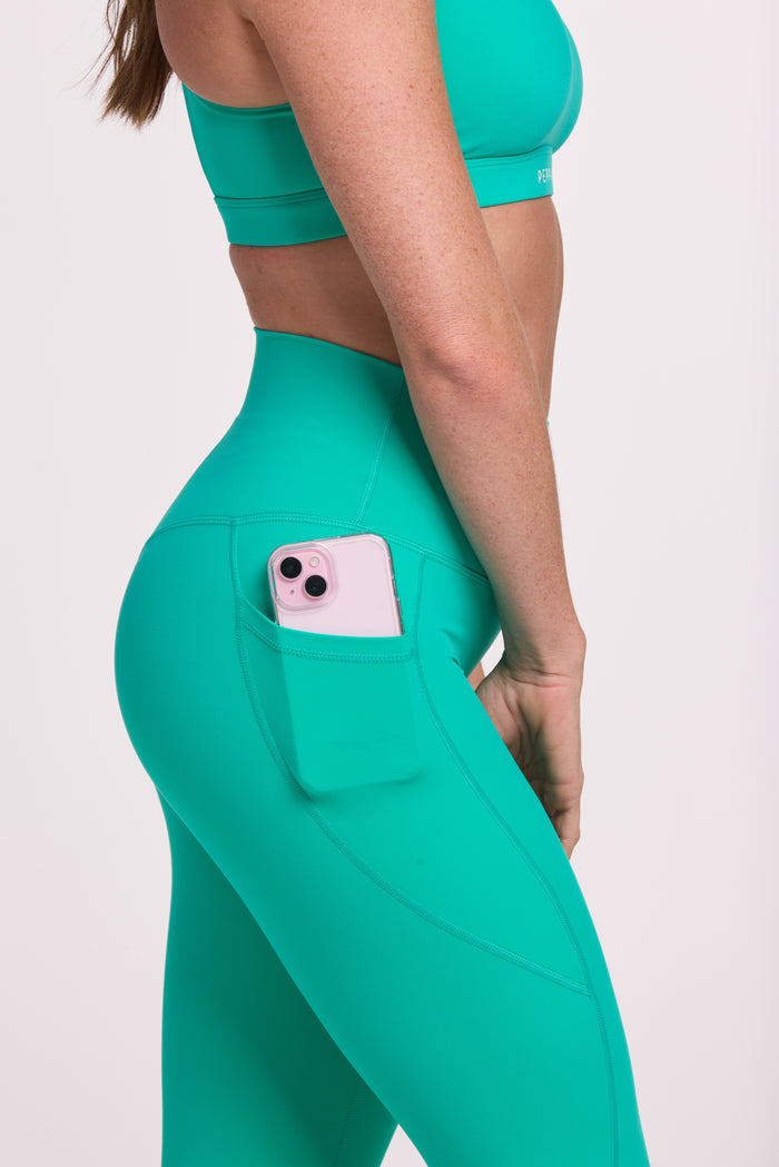 Buttery soft high waisted women's gym tights with practical pockets,  sweetheart back seams for an upper glute shaping effect, and no front rise seam paired with a high neck women's sports bra with a supportive elasticated hem and triple layered fabric with removable pads for extra support and crossover back straps in cyan green
