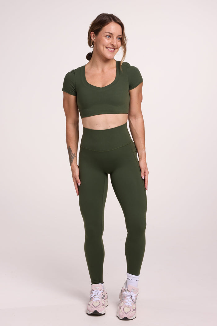 Buttery soft high waisted women's gym tights with practical pockets, sweetheart back seams for an upper glute shaping effect, and no front rise seam, paired with an V neck women's crop t-shirt with a supportive elasticated hem and triple layered fabric with removable pads for extra support in forest green