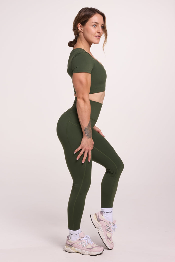 Buttery soft high waisted women's gym tights with practical pockets, sweetheart back seams for an upper glute shaping effect, and no front rise seam, paired with an V neck women's crop t-shirt with a supportive elasticated hem and triple layered fabric with removable pads for extra support in forest green