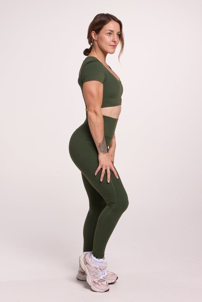 Buttery soft high waisted women's gym tights with practical pockets, sweetheart back seams for an upper glute shaping effect, and no front rise seam, paired with an V neck women's crop t-shirt with a supportive elasticated hem and triple layered fabric with removable pads for extra support in forest green