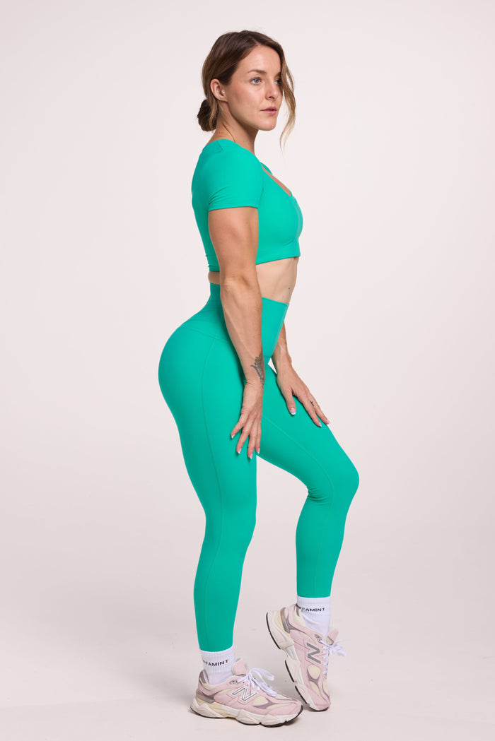 Buttery soft high waisted women's gym tights with curved back seam stitched detailing for a butt shaping effect, and no front rise seam paired with an V neck women's crop t-shirt with a supportive elasticated hem and triple layered fabric with removable pads for extra support in cyan green