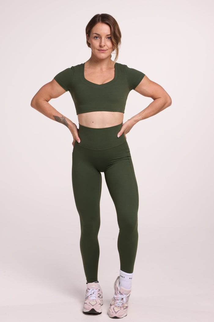 Buttery soft high waisted women's gym tights with practical pockets, sweetheart back seams for an upper glute shaping effect, and no front rise seam, paired with an V neck women's crop t-shirt with a supportive elasticated hem and triple layered fabric with removable pads for extra support in forest green