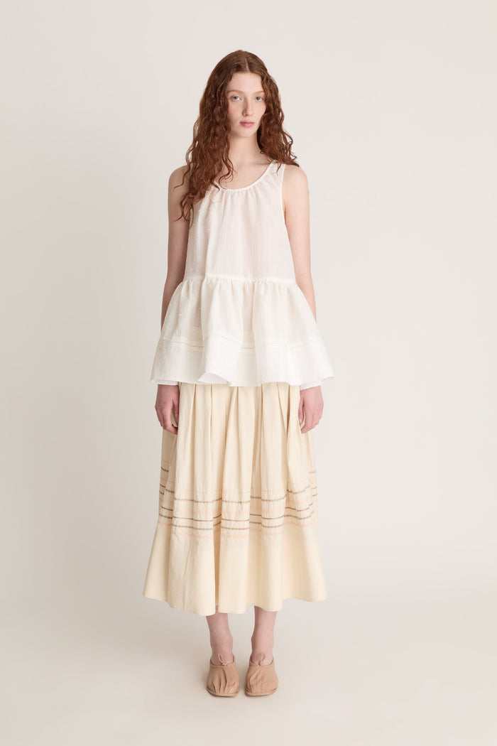 A woman wearing a white top with a peplum with a beige skirt on a white background