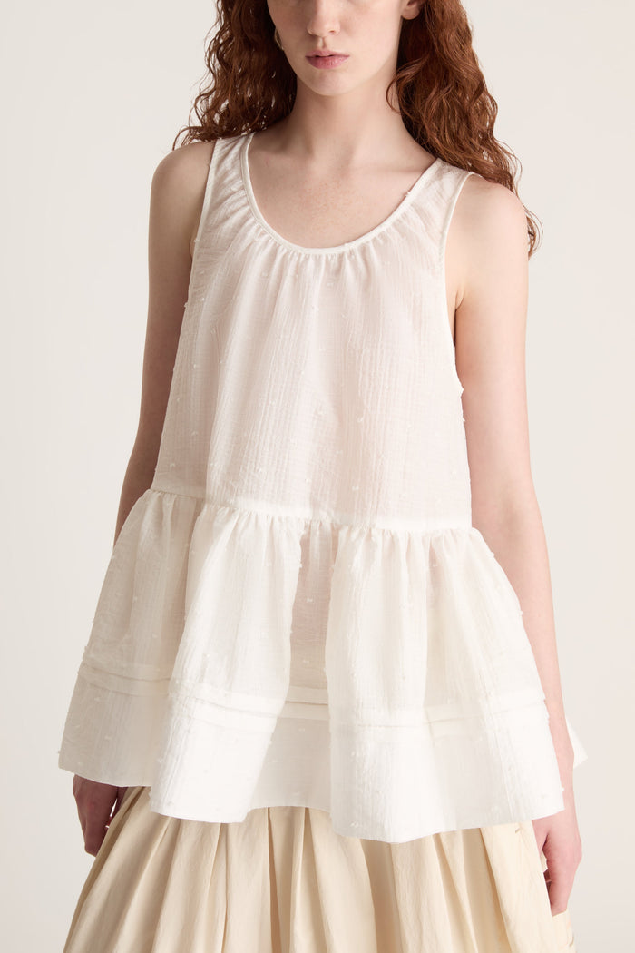 A woman wearing a white top with a peplum with a beige skirt on a white background