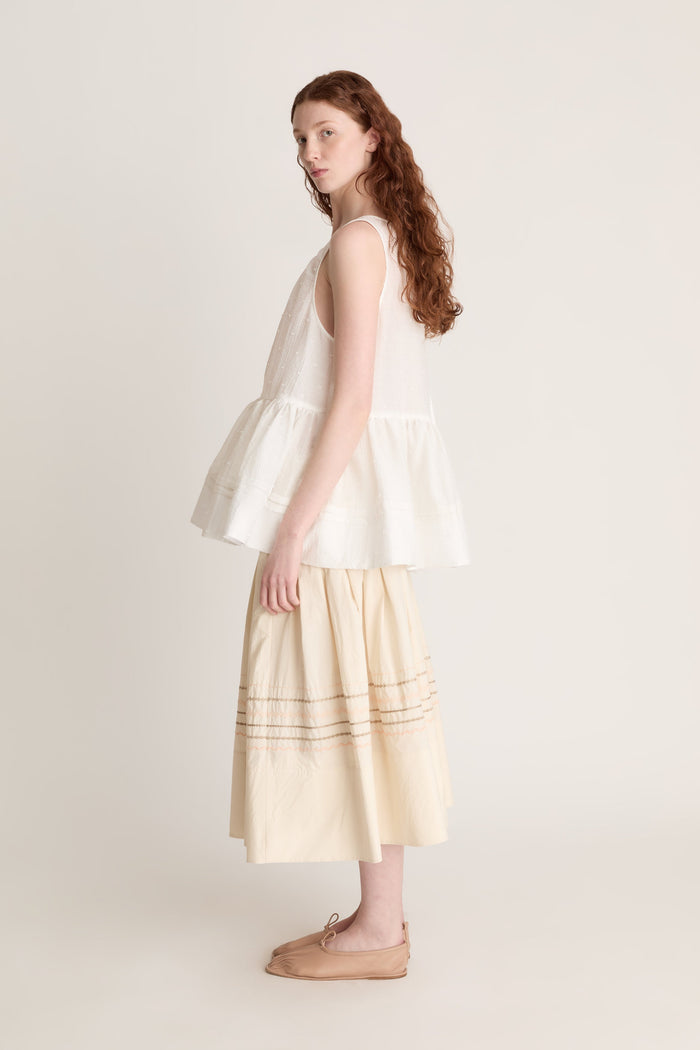 A woman wearing a white top with a peplum with a beige skirt on a white background