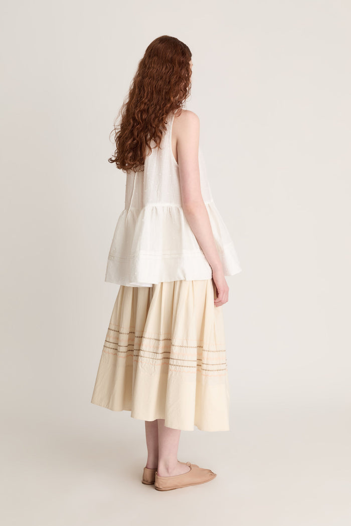 A woman wearing a white top with a peplum with a beige skirt on a white background