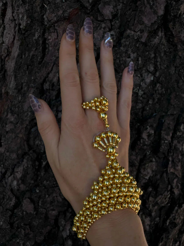 luxury beaded hand jewelry with 22k gold wash on polymer metal beads on hand with wood background by object and dawn