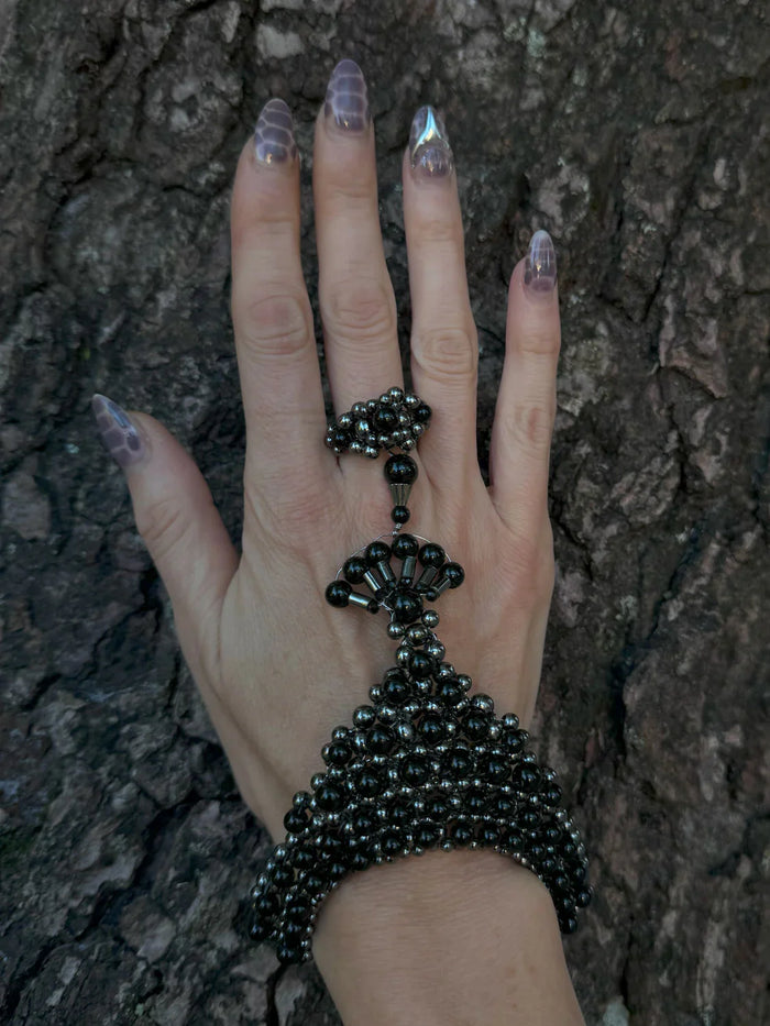 handcrafted beaded hand jewelry polymer metal beads and crystal black on hand with wood background by object and dawn