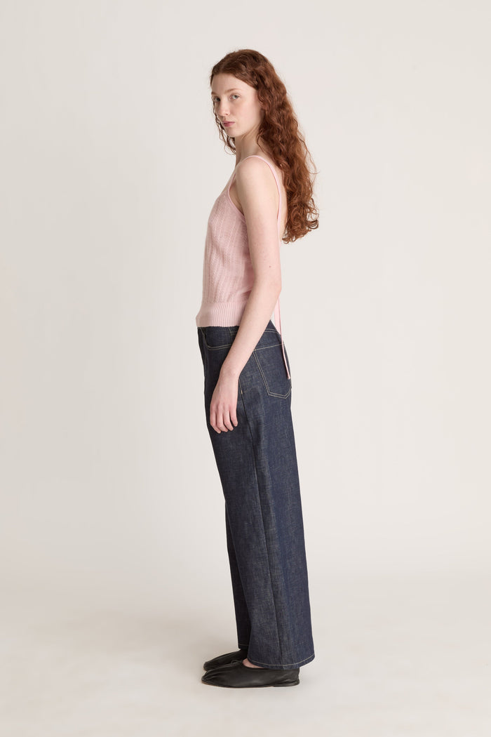 Woman wearing a pink knit top and dark blue jeans on a white background