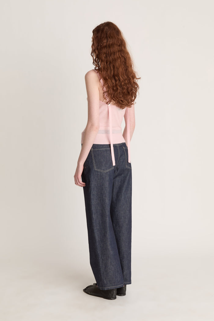 Woman wearing a pink knit top and dark blue jeans on a white background