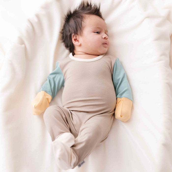 Baby lying on a white blanket wearing a beige and blue outfit.
