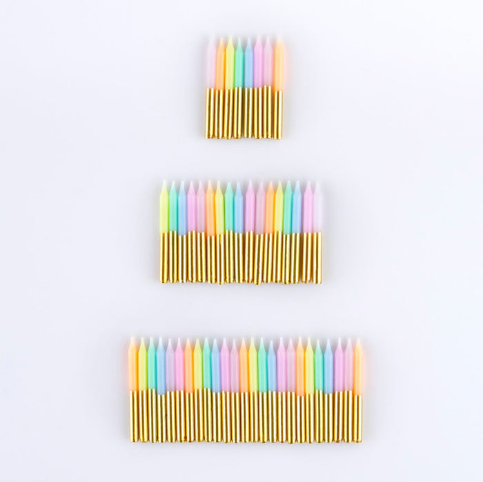 Three sets of colorful birthday candles arranged vertically on a plain white background. The candles have pastel pink, yellow, green, blue, and orange tips with shiny gold wax bases.