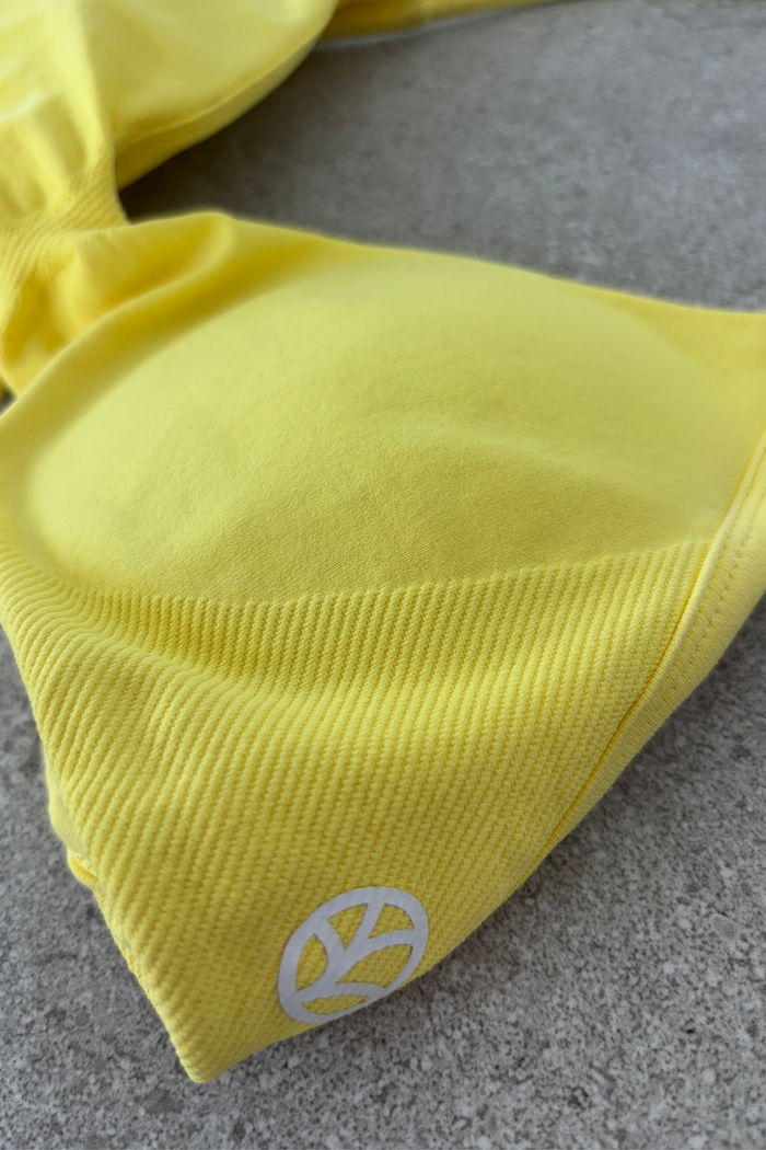 Minimalistic bra with breast contouring panels and a ruched front seam to effortlessy shape the breasts, with a sleek back straps and halter neck design for showcasing the back gains in buttercup yellow