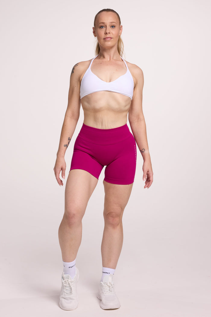 Minimalistic bra with breast contouring panels and a ruched front seam to effortlessly shape the breasts, with a sleek back straps and halter neck design in white and seamless gym tights with booty contouring panels, invisible scrunch technology, sweetheart shaped back seams and thick supportive fabric in magenta colour
