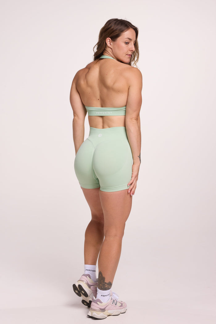 Seamless halter bra with a thick supportive fabric blend and a branded back strap, with a ribbed elastic hem and seamless gym shorts with booty contouring panels, invisible scrunch technology, sweetheart shaped back seams and thick supportive fabric in mist green