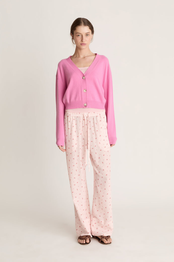 Woman wearing pink cashmere cardigan and pink floral pants on a white background