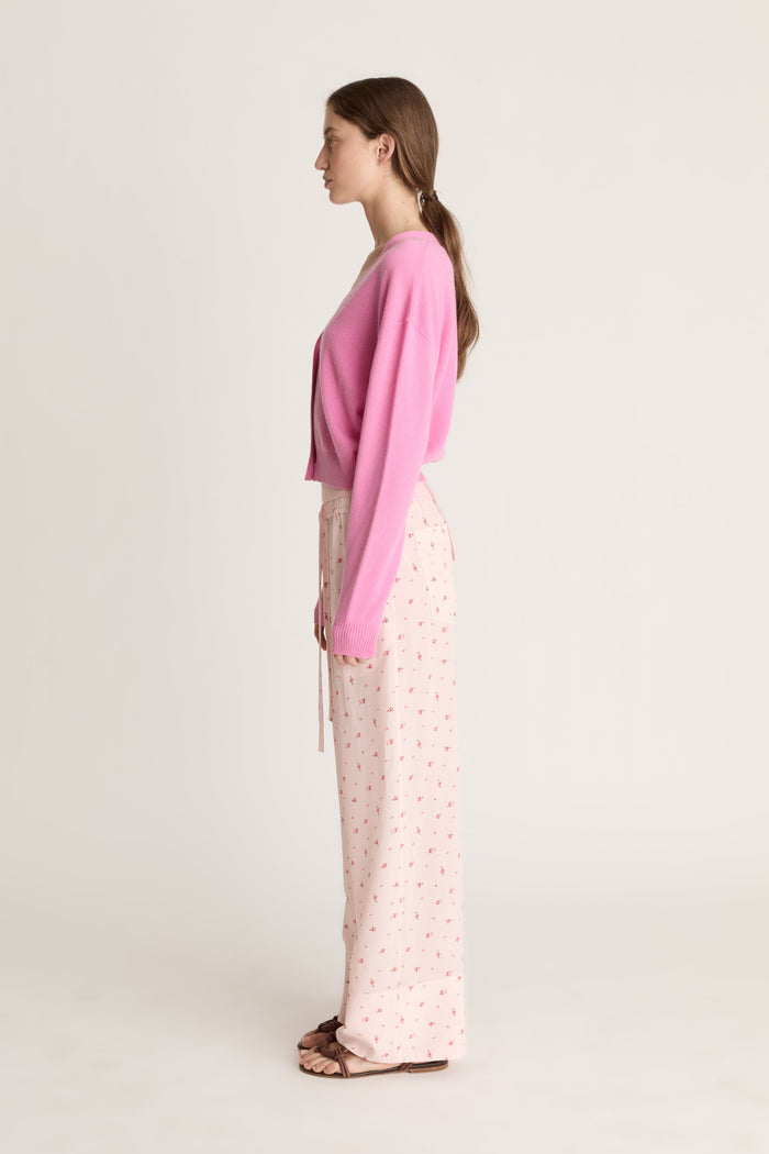Woman wearing pink cashmere cardigan and pink floral pants on a white background