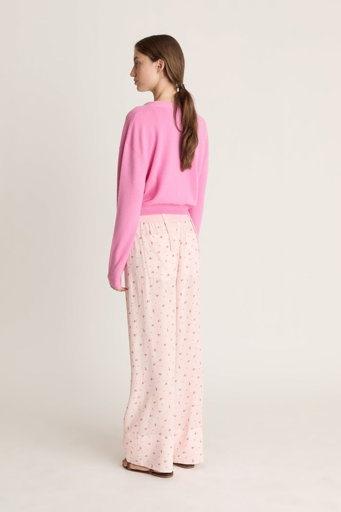 Woman wearing pink cashmere cardigan and pink floral pants on a white background