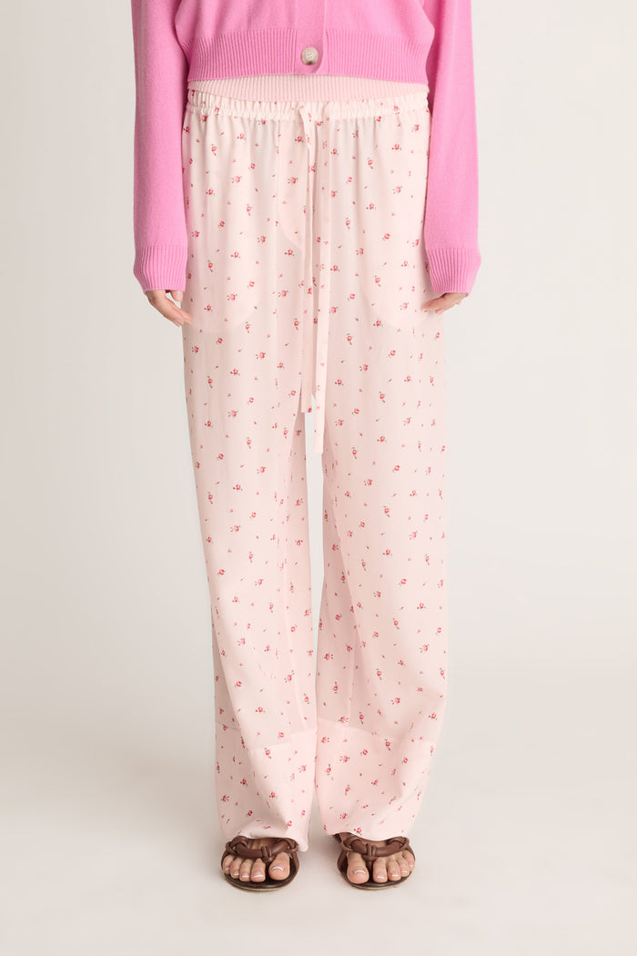 Woman wearing pink cashmere cardigan and pink floral pants on a white background