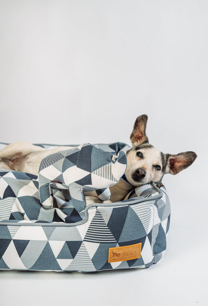 Dog laying in a Mosaic Lounge Bed in Tuxedo on a white background snuggling P.L.A.Y. Upcycled Zoo Pal Rhino plush toy inside it