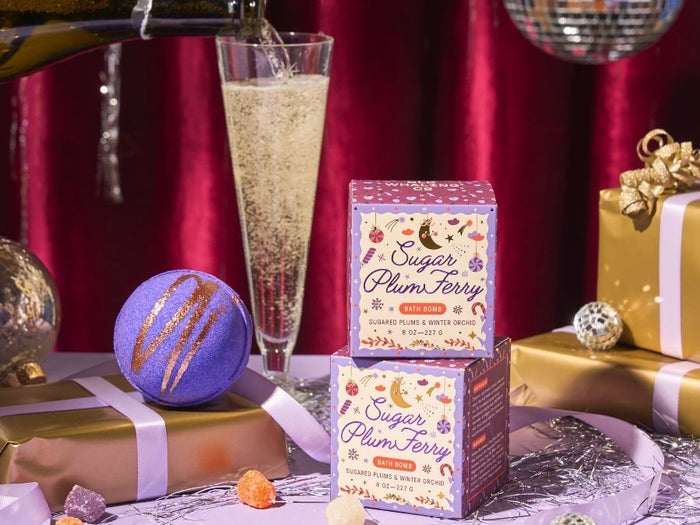 Two boxes of 'Sugar Plum Fairy' bath bombs on a festive table with champagne and gift boxes.